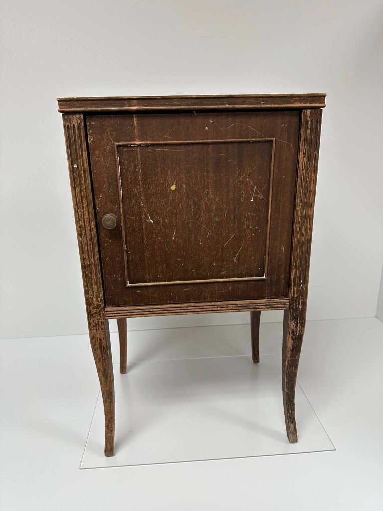 A distressed dark brown wooden cabinet with a single door and curved legs stands against a white background.