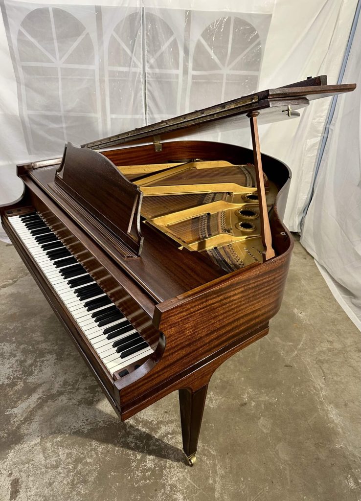 A polished dark wood grand piano with its lid open, showcasing the internal strings and keys.