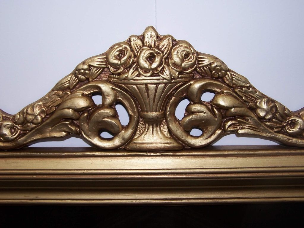 An ornate antique gold picture frame top features carved roses, scrolling leaves, and a central