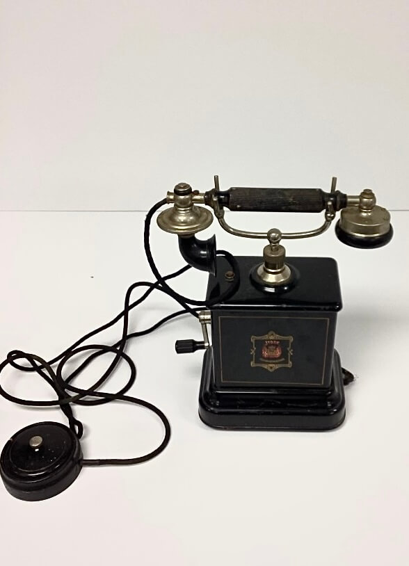 An antique black crank telephone with a separate earpiece and mouthpiece sits on a white surface.