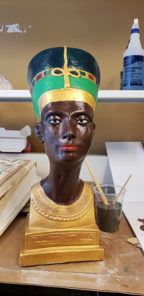 A detailed, painted bust of Nefertiti with a dark complexion, gold collar