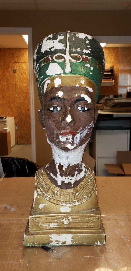 A dark-skinned Nefertiti bust with peeling paint and white restoration material. TITLE