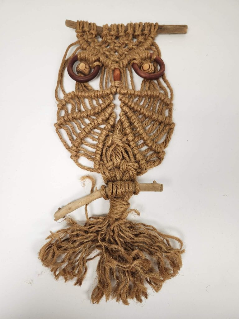 A brown macrame owl wall hanging features wooden ring eyes and a natural branch perch. TITLE
