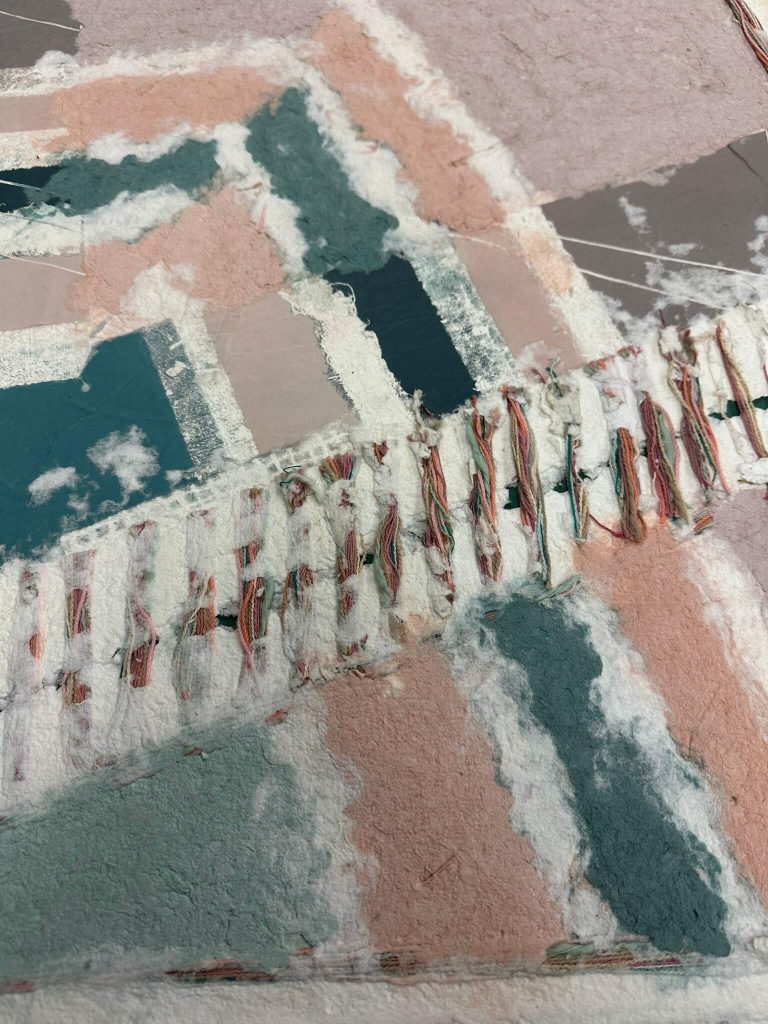 Textured abstract collage of torn paper in muted pink, teal, and white, with