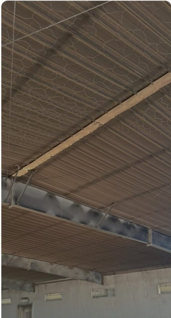 Corrugated metal ceiling with chicken wire mesh, a wooden beam, and ventilation ducts