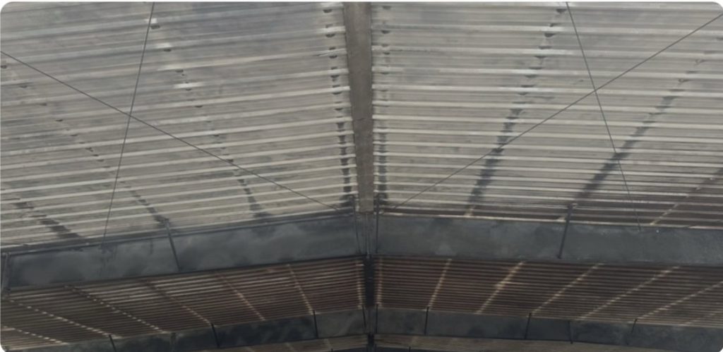 Underside view of a corrugated roof with dark beams and crisscrossing wires.