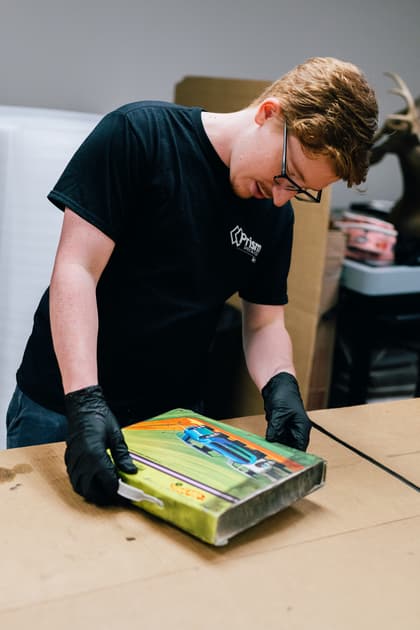 A man in black gloves carefully inspects a colorful race car art piece on a table.