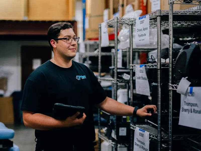 Prism employee reviewing labeled warehouse shelving with a tablet