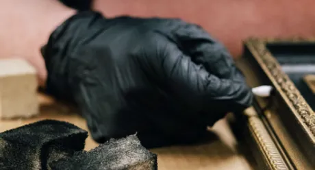 Gloved hands cleaning a gilded picture frame with a cotton swab