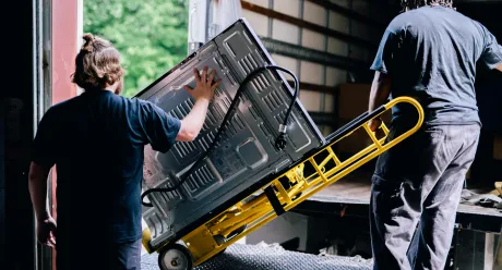 Two technicians loading a flat-screen TV onto a hand truck