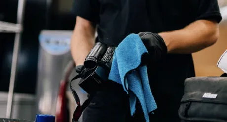Technician cleaning a video camera with a blue cloth