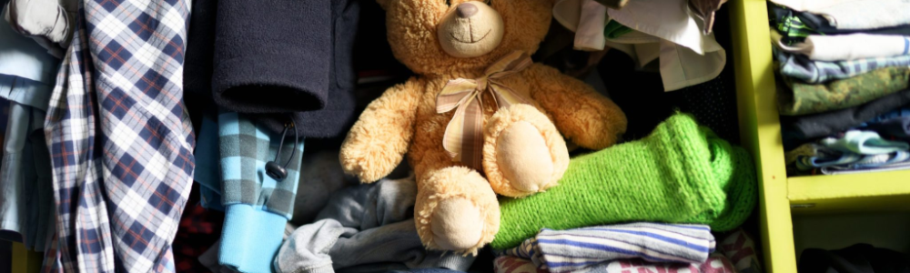Teddy bear among clothing in a closet