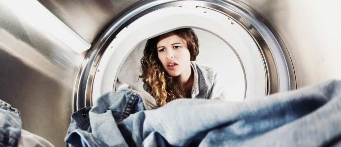 Woman is pulling clothes out of the dryer. She has an unpleasant look as she inspects the clothing.