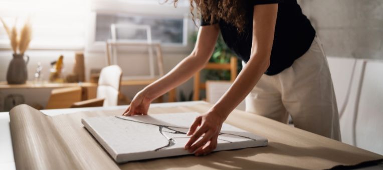 Young woman placing a painting on top of thick padding material to wrap it in.
