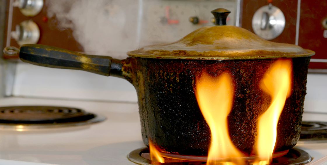 A dirty pot surrounded in flames on an electric stove top