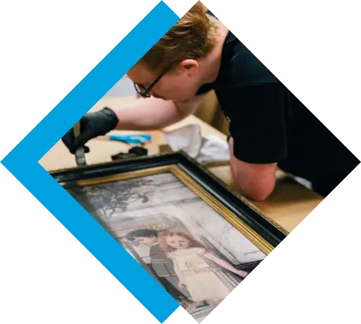 A conservator wearing black gloves meticulously restores a vintage framed portrait of two children. TITLE: