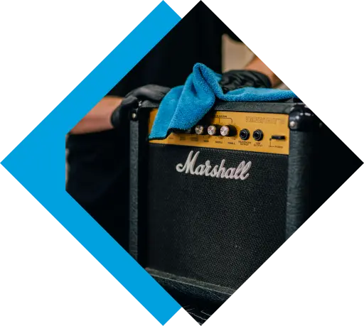 A person cleans a black Marshall guitar amplifier with a blue microfiber cloth.