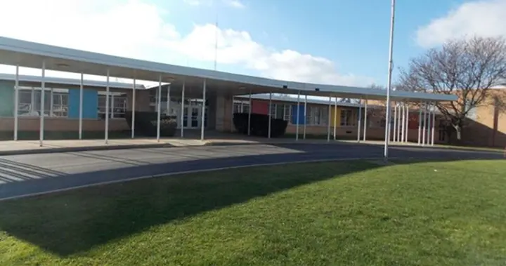 Modern school building with a long covered entrance, colorful panels, and a green lawn under a