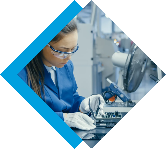 A technician in safety glasses and gloves precisely works on an electronic circuit board.