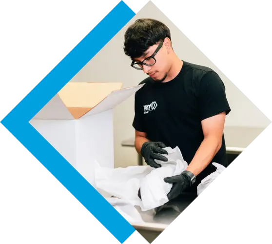 A man wearing gloves carefully packs an item into a white box.