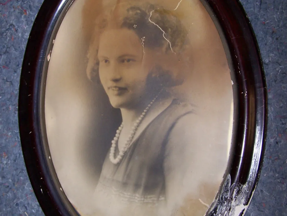 Old sepia portrait of a woman with pearls in a distressed oval wooden frame.