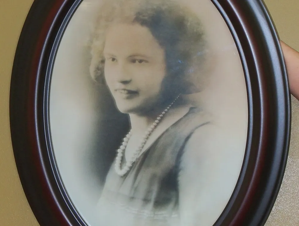 Black and white portrait of a smiling woman with curly hair and a pearl necklace in an oval