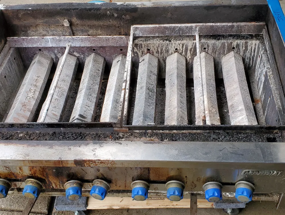A dirty commercial Imperial range with hexagonal grates and blue-capped control knobs. TITLE: