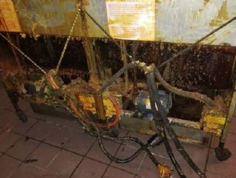 The underside of a commercial kitchen appliance is heavily caked with thick, dark grease and