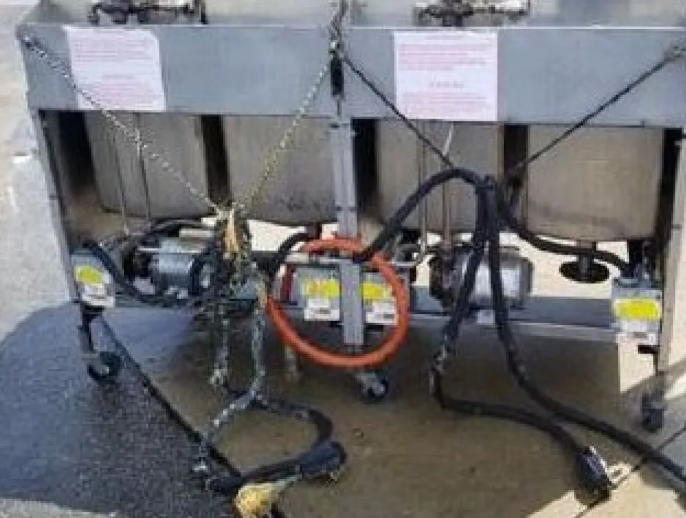 A stainless steel commercial double-vat unit with pumps, hoses, and electrical connections on
