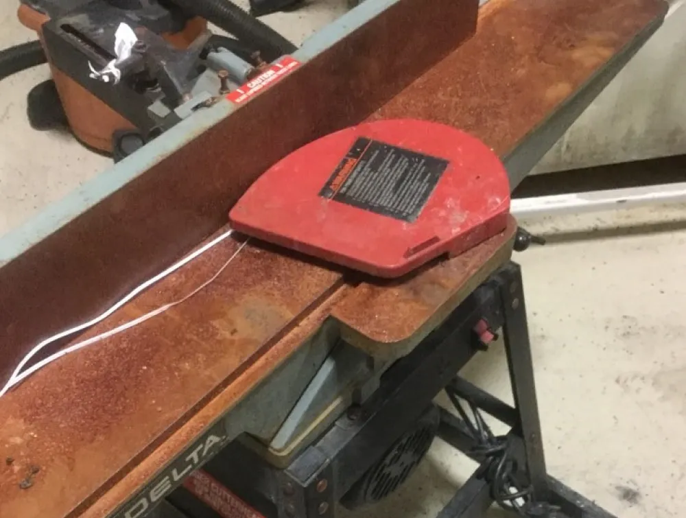 Heavily rusted Delta woodworking jointer with a red blade guard and white string on its surface.