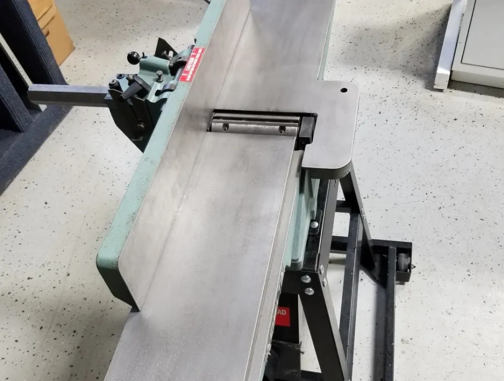 A woodworking jointer machine with a long metal bed and an adjustable fence.